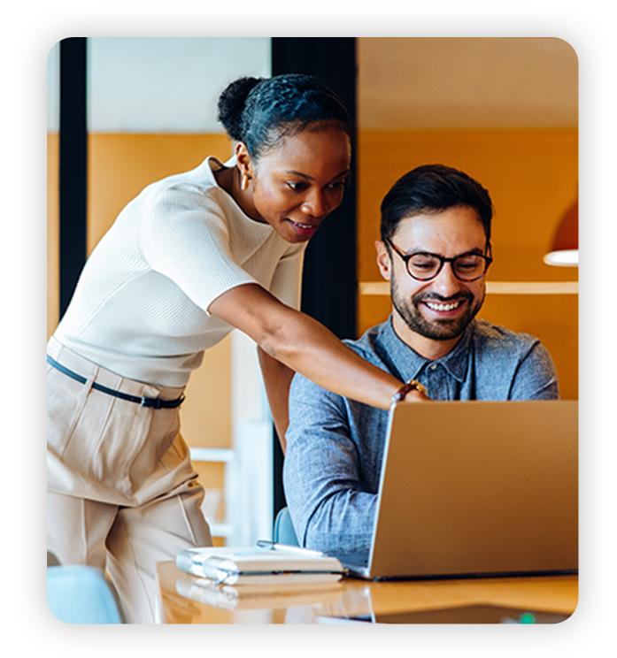 Two excited coworkers work on laptop in modern office